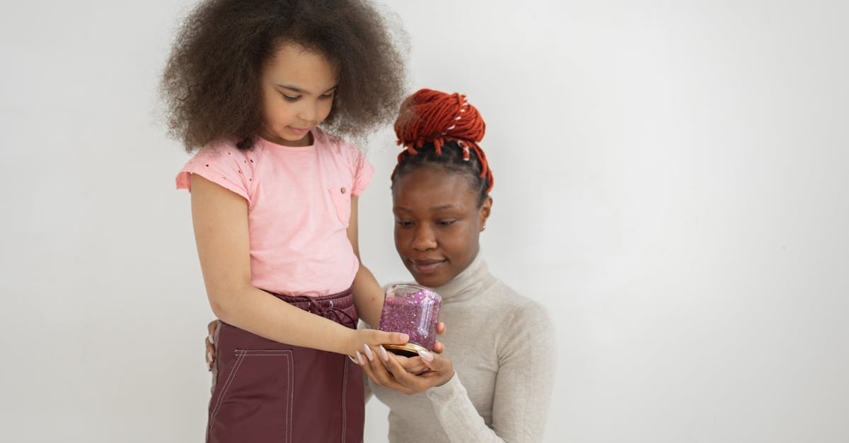 cute african american little girl with dark curly hair standing near white wall and showing mother j 1