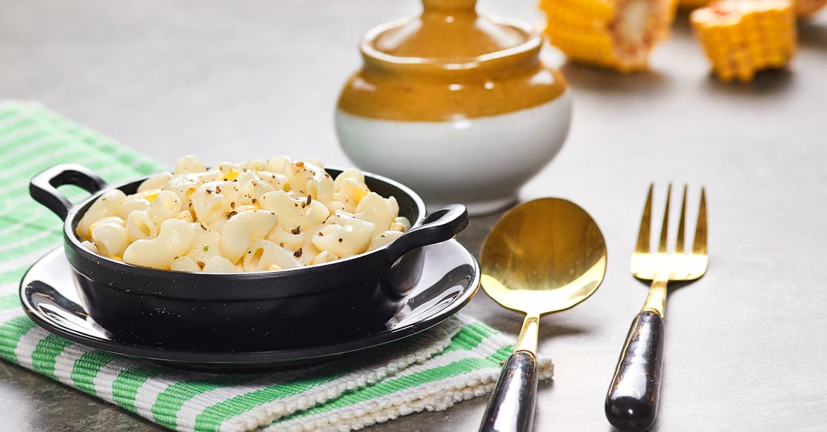 delicious creamy macaroni with corn served in a black bowl alongside cutlery on a checkered cloth 3