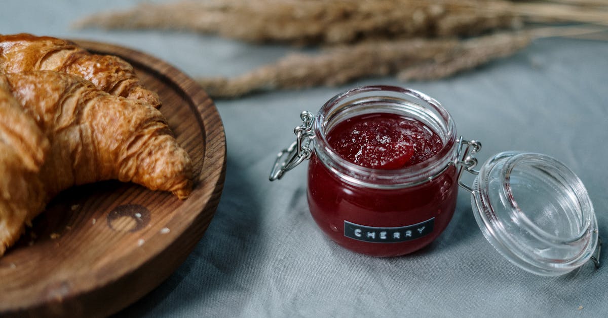 delicious croissants on wooden plate with cherry jam jar on rustic table