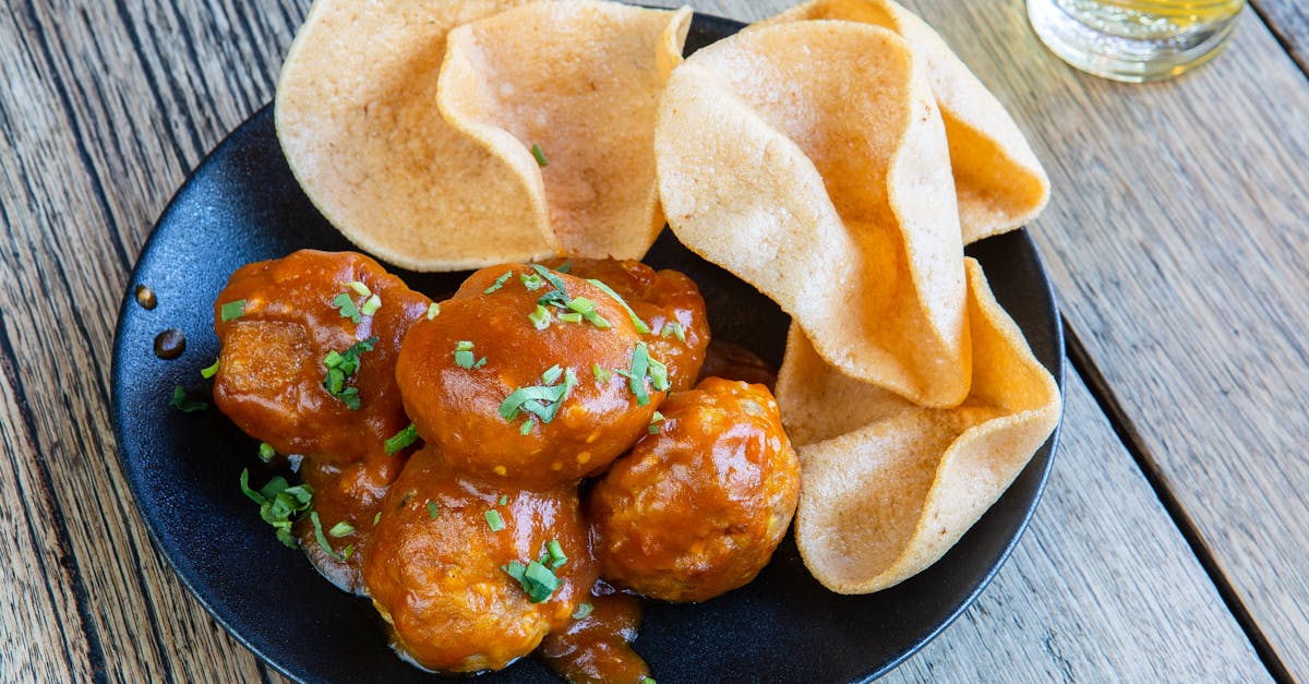 delicious meatballs in sweet and spicy sauce served with crispy chips on a wooden table