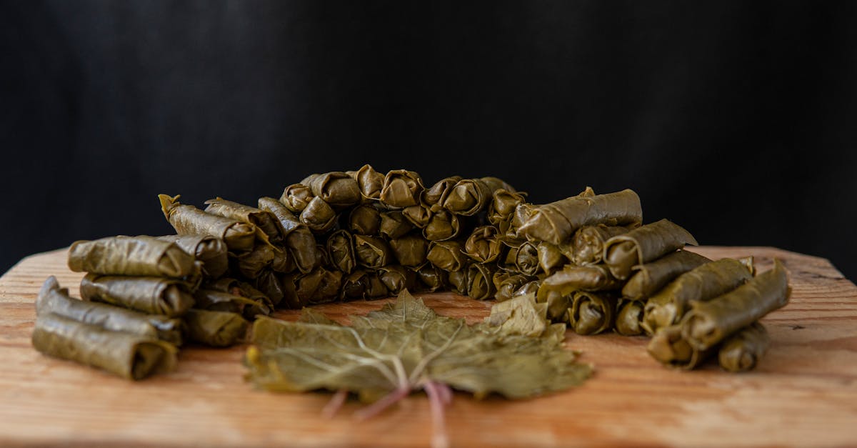 delicious sarma rolls near vine leaf on wooden cutting board on black background