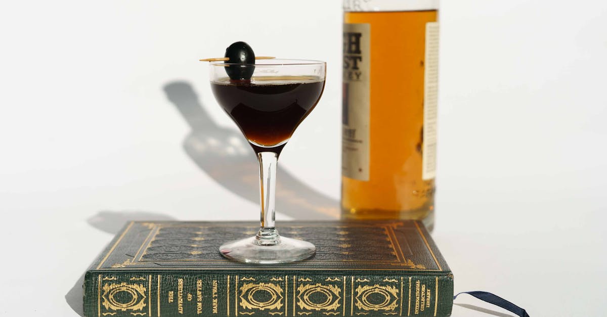 elegant cocktail with an olive on a toothpick set on a vintage book with a whiskey bottle in the ba 13