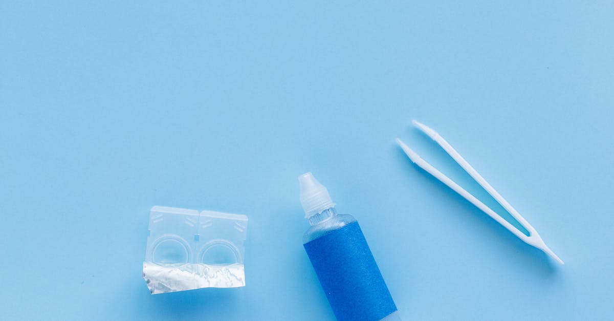 flat lay of contact lenses solution bottle and tweezers on a blue background
