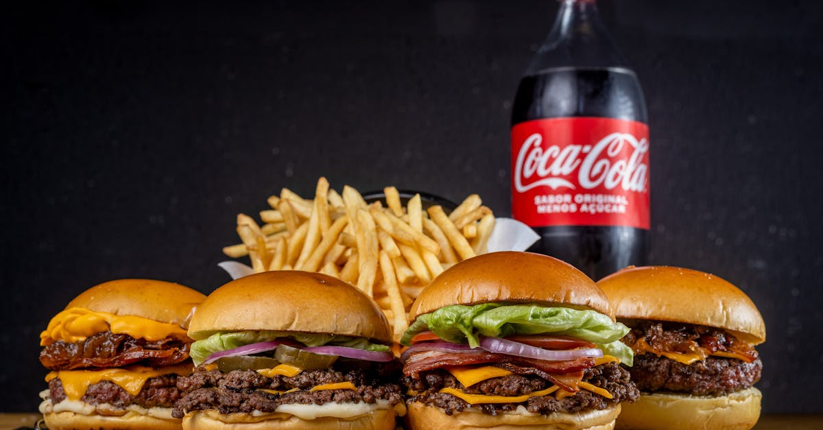 four gourmet burgers with fries and a bottle of coca cola create the perfect meal