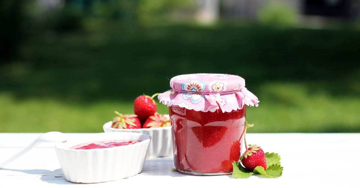 fresh homemade strawberry jam in a decorative jar with ceramic bowls on a white table outdoors 6