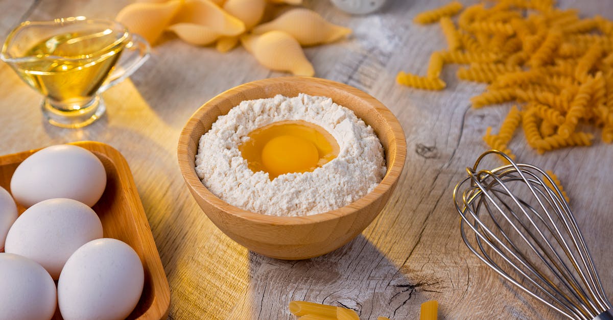 fresh ingredients for homemade pasta eggs flour oil and whisk on a wooden table