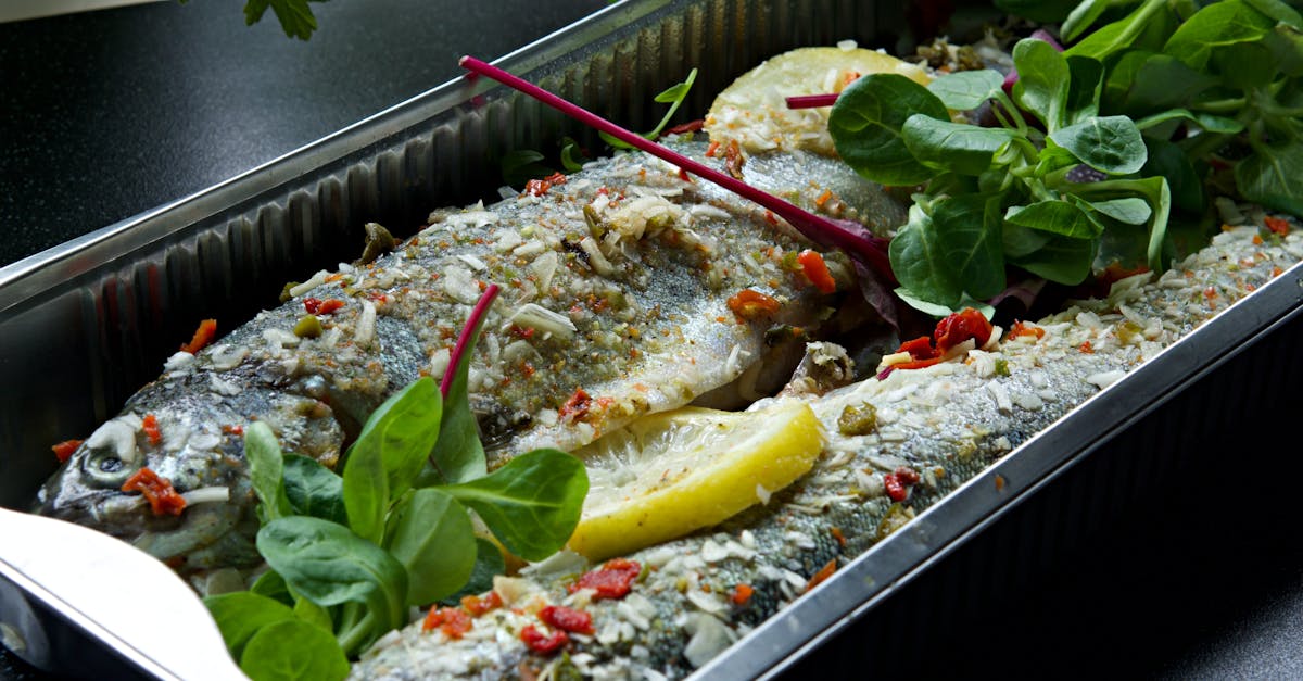 freshly baked trout in an aluminum tray garnished with lemon herbs and spices