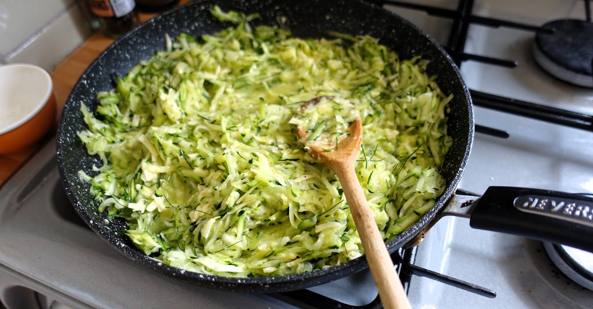 freshly shredded zucchini cooking in a frying pan on a modern kitchen stove