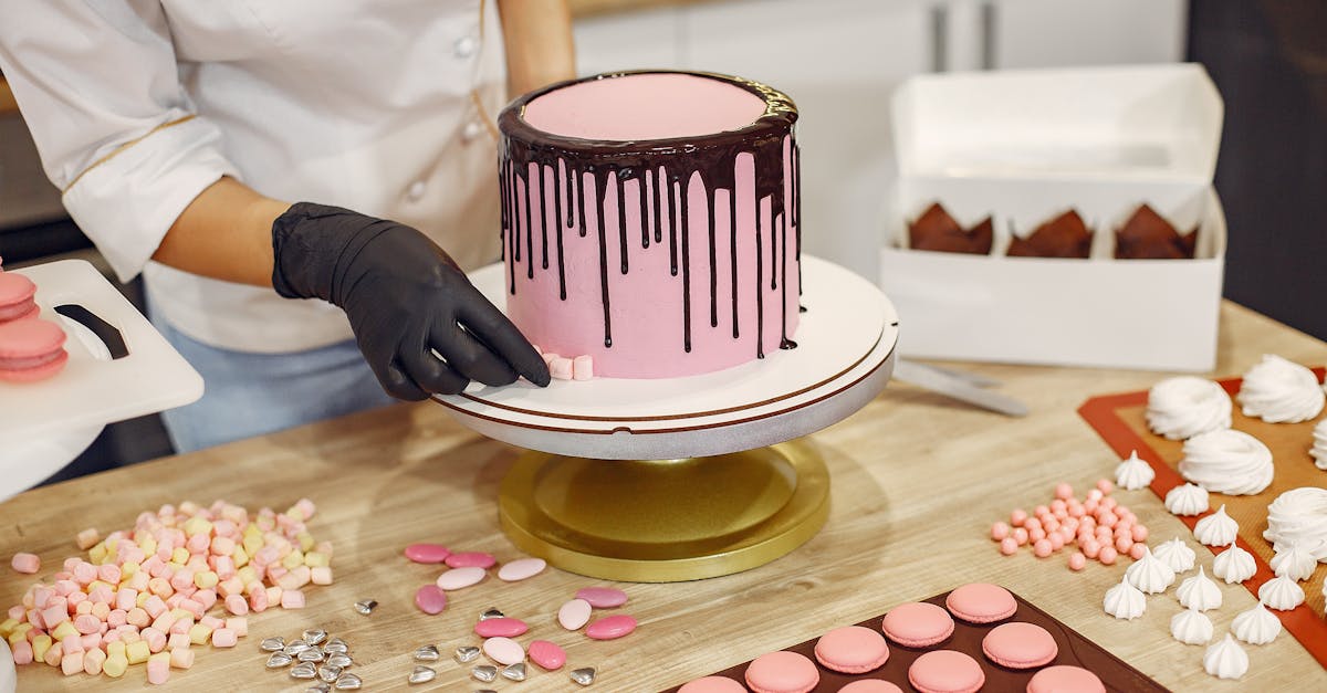 from above crop female cook in uniform and latex gloves placing small sweets on bottom of cake place 2