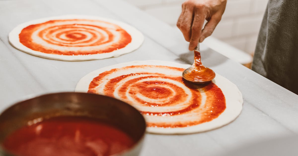 hand spreading tomato sauce on pizza dough in an indoor setting