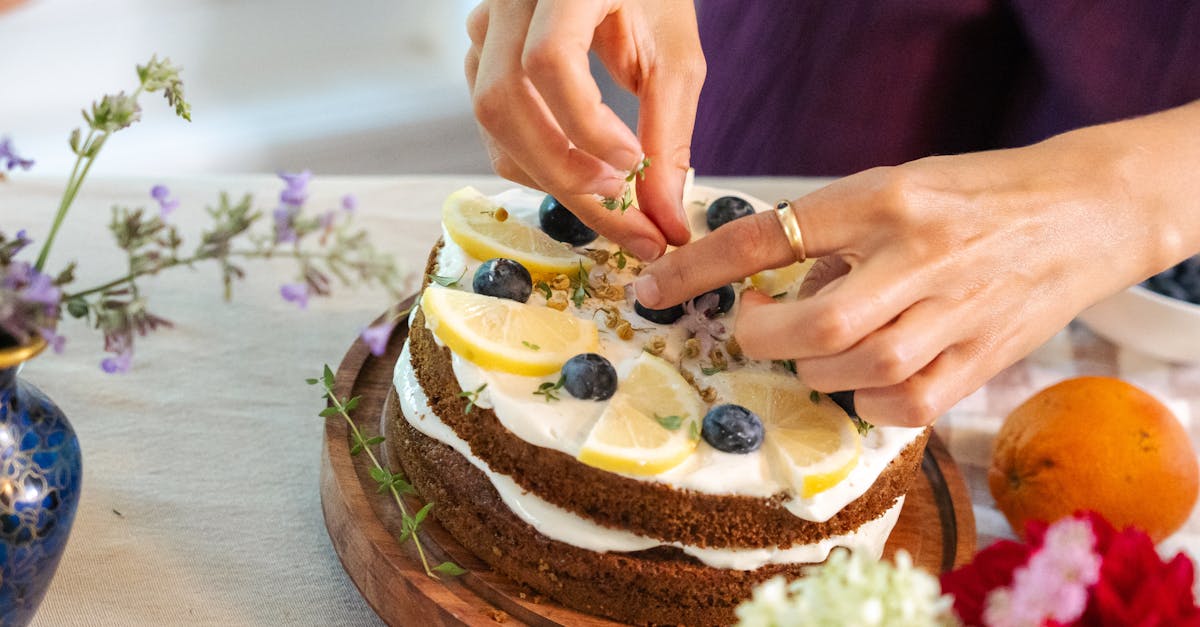 hands decorating a lemon blueberry cake with herbs surrounded by fresh flowers