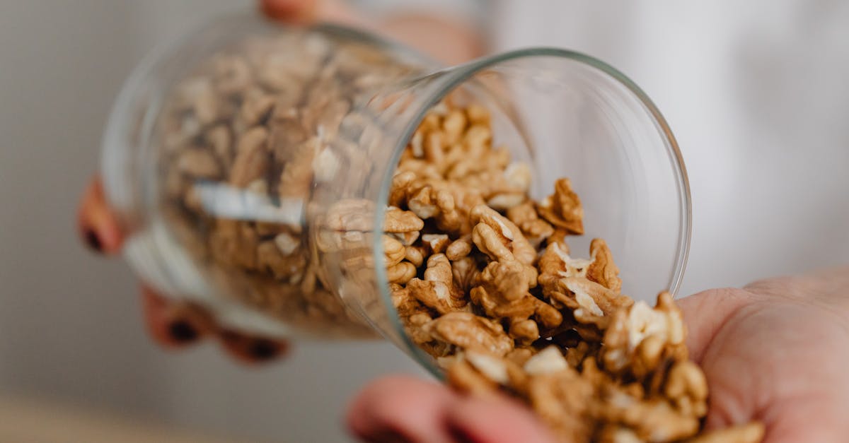 hands pouring walnuts from a glass jar featuring a rustic kitchen scene
