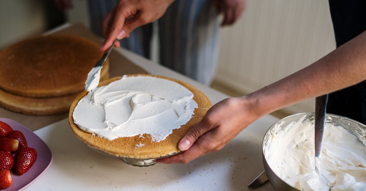 hands preparing a cake with cream frosting in a cozy kitchen setting featuring strawberries and a m 6