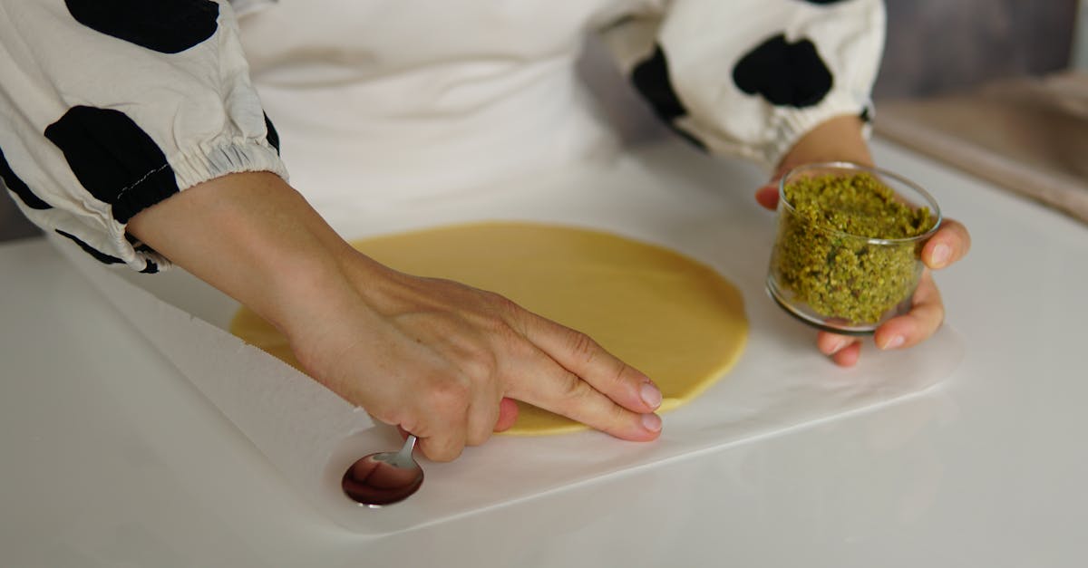 hands preparing dough with pistachio filling on parchment paper