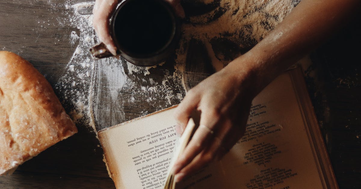 hands with coffee cup and recipe book on flour dusted table with bread 1