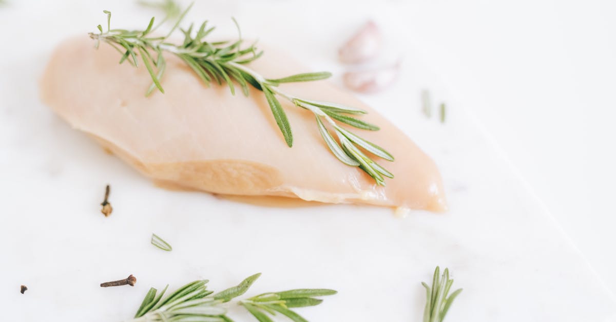 healthy raw chicken breast garnished with rosemary on a marble surface
