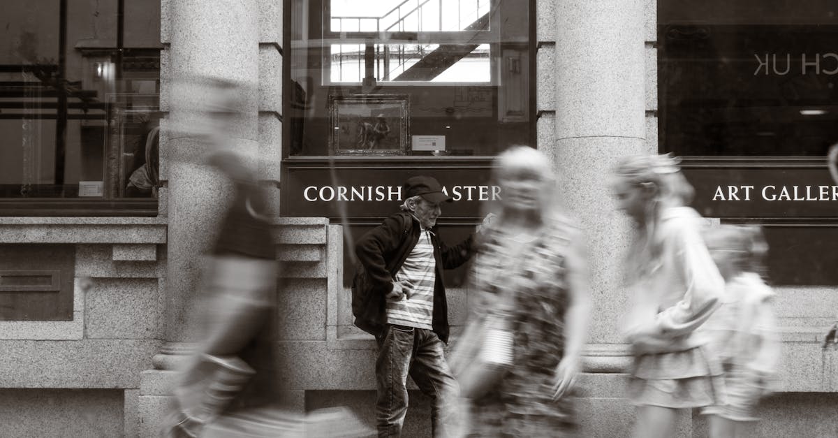 man standing against art gallery as blurred pedestrians pass by in grayscale