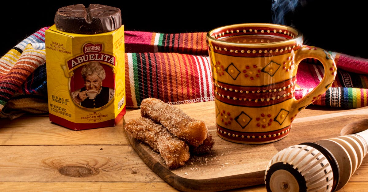 mexican hot chocolate with churros on a wooden board served with a molinillo and colorful blanket