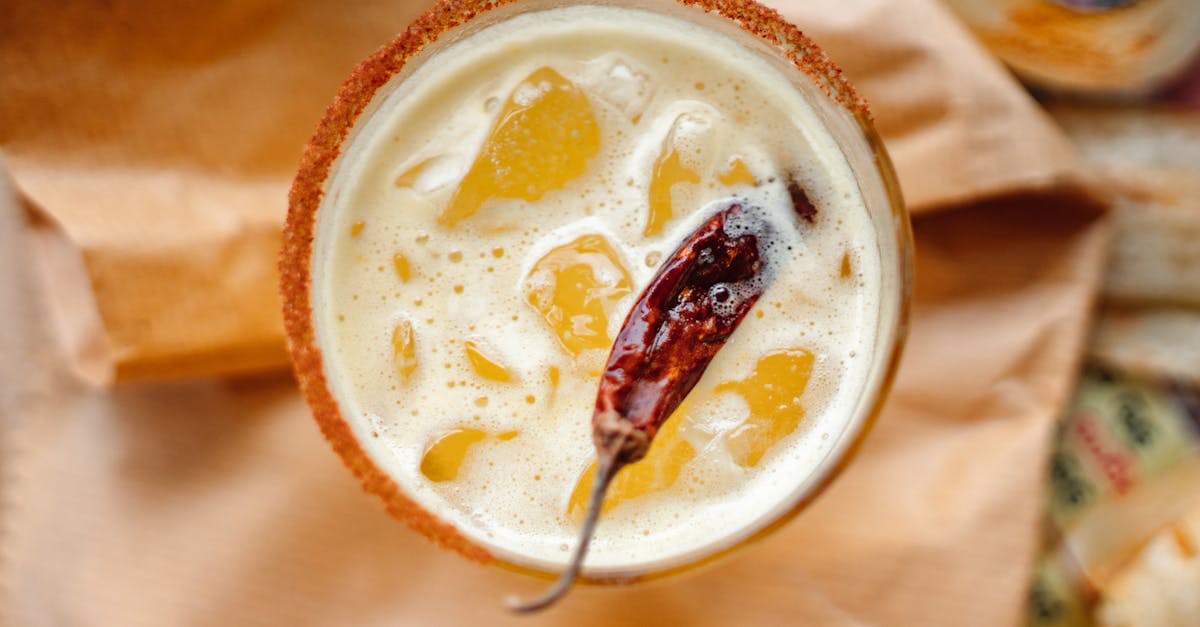 overhead view of a spicy iced beverage garnished with a whole chili pepper on a textured brown surfa