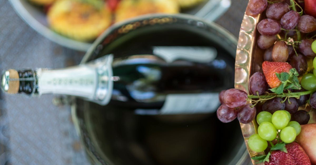 overhead view of champagne bottle in ice bucket with fresh grapes and fruit platter on a sunny day