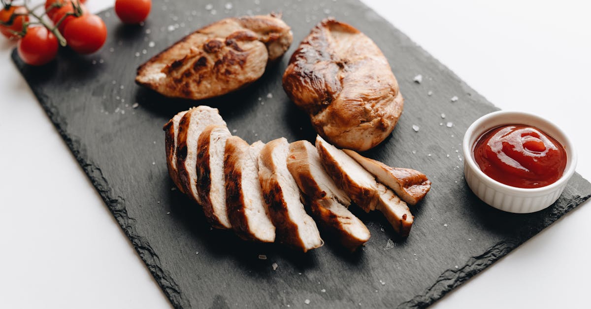 sliced grilled chicken breast on slate with cherry tomatoes and dipping sauce