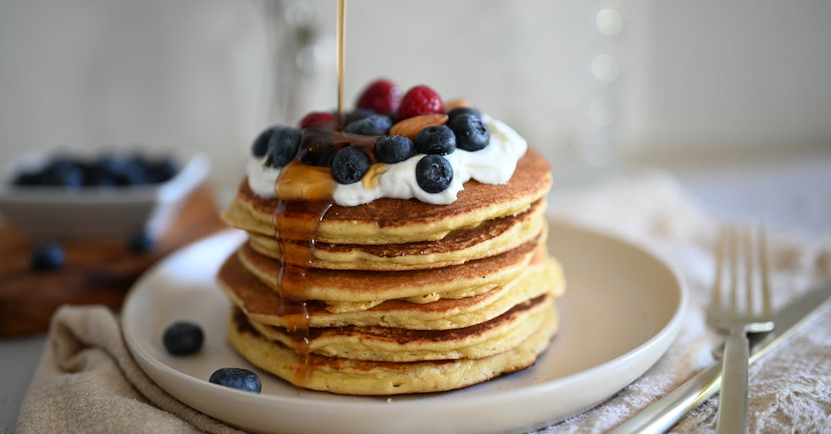 stack of pancakes with blueberries and raspberries topped with syrup and whipped cream on a plate 1