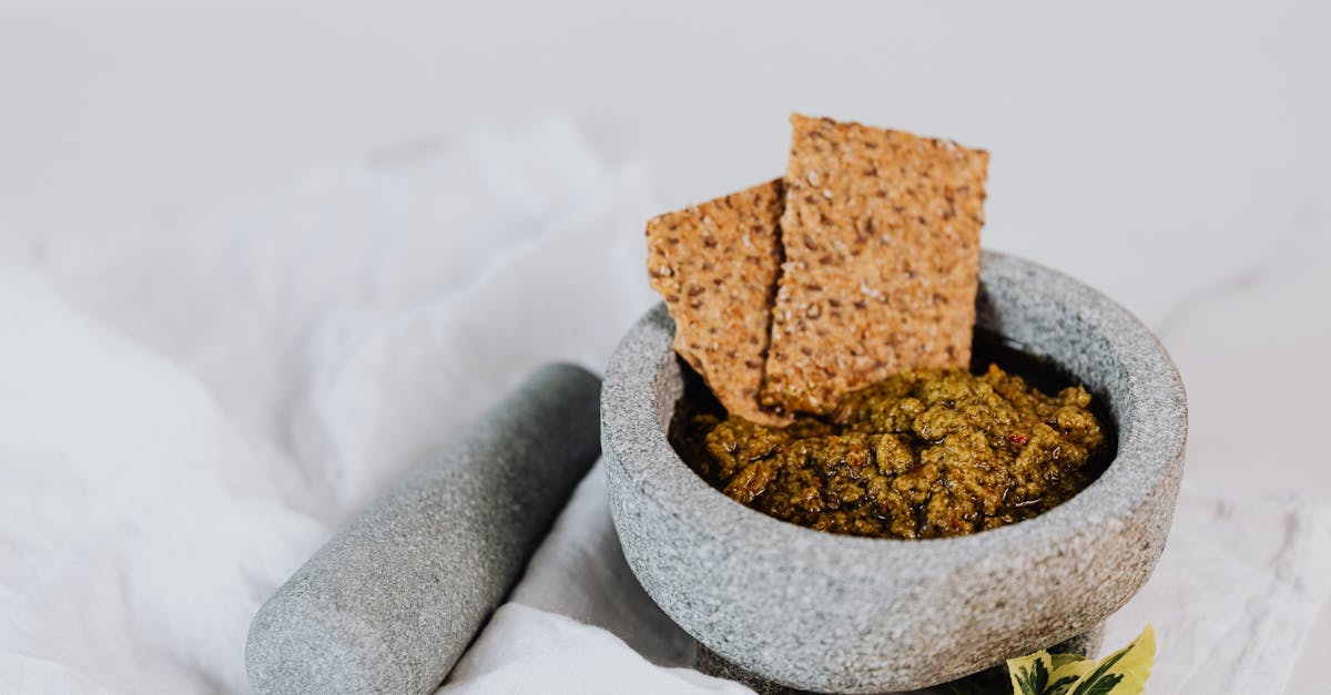 stone mortar and pestle with fresh green pesto and crispbreads on white cloth 1