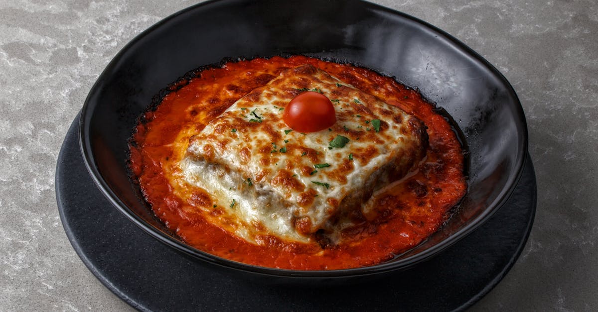 tasty baked lasagna with cherry tomato and cheese served in a black bowl with rich tomato sauce 3