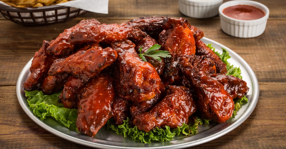tasty bbq chicken wings served with green lettuce and dipping sauces on a wooden table