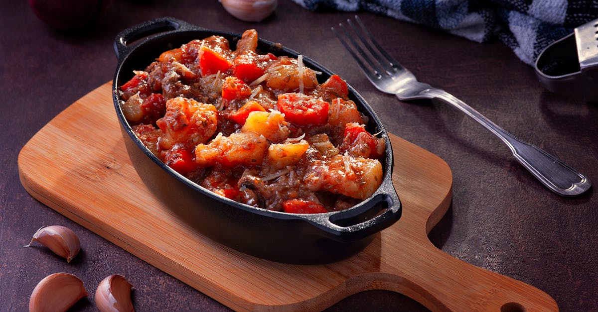 tasty vegetable stew with garlic and tomatoes in a black casserole dish on a wooden board