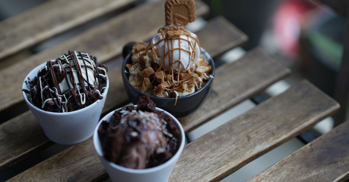 three bowls of delicious ice cream with chocolate drizzle and cookies on a wooden table