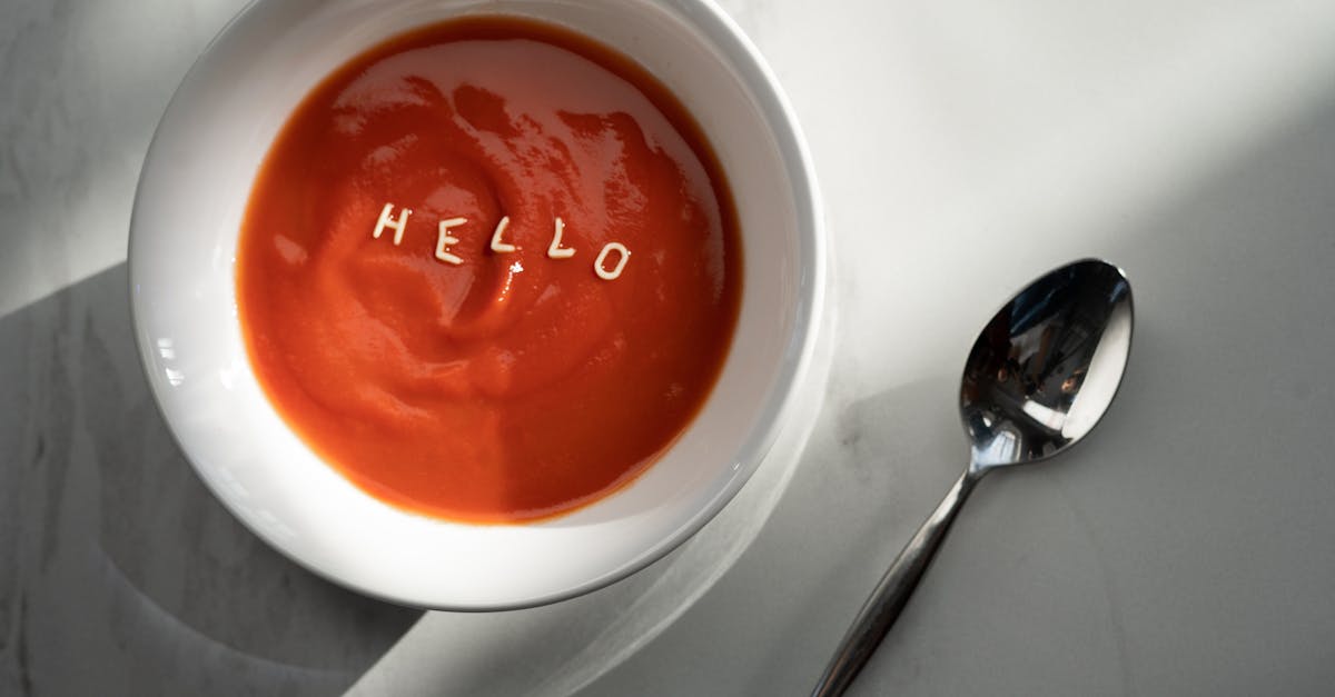 tomato soup in a bowl with the word hello formed by pasta letters alongside a spoon