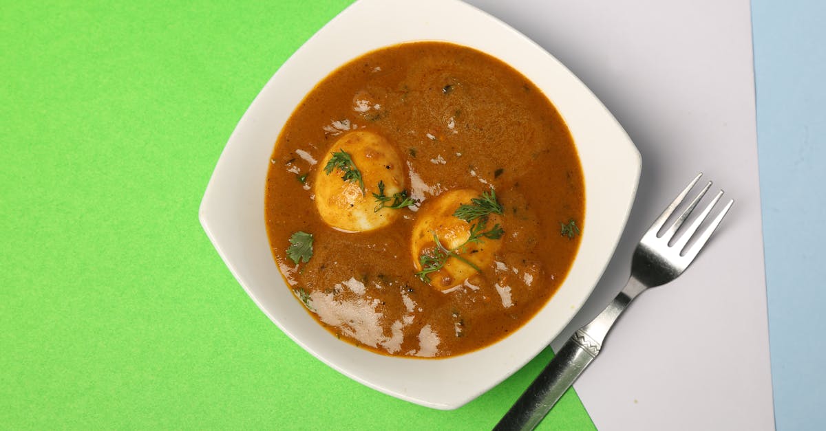 top view of a savory egg curry in a white bowl styled on a vibrant green and blue backdrop