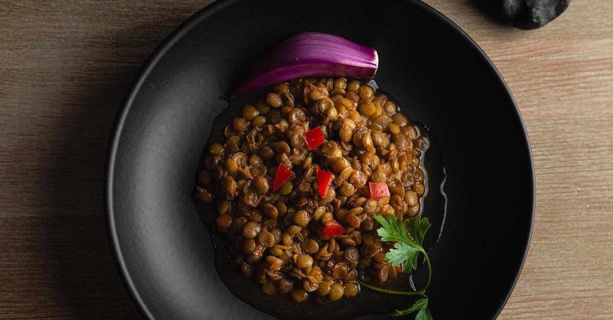 top view of a savory lentil dish garnished with onion and parsley in a black bowl