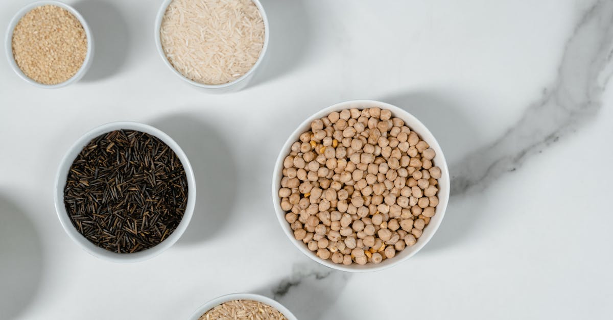 top view of assorted grains and lentils in white bowls on a marble surface for culinary concepts