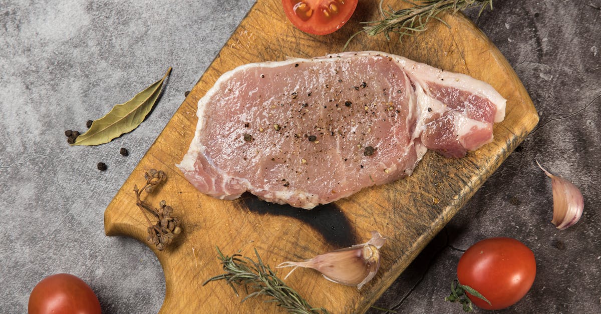 top view of raw pork steak on a wooden board with fresh herbs and tomatoes