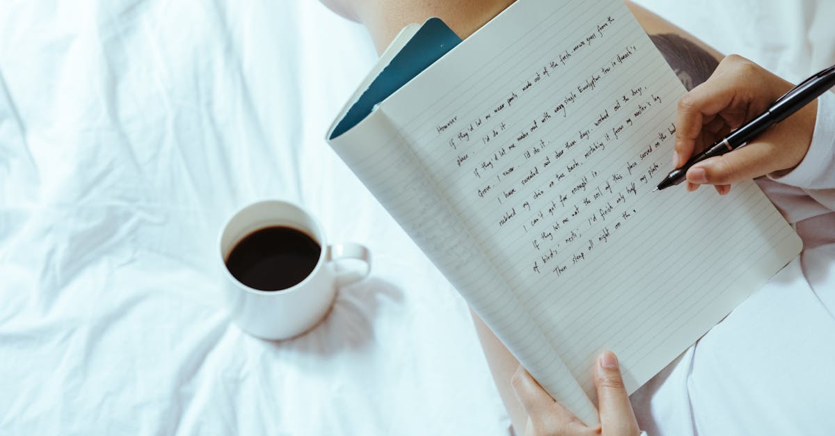 top view of unrecognizable woman sitting on bed with legs near cup of coffee and writing on notepad