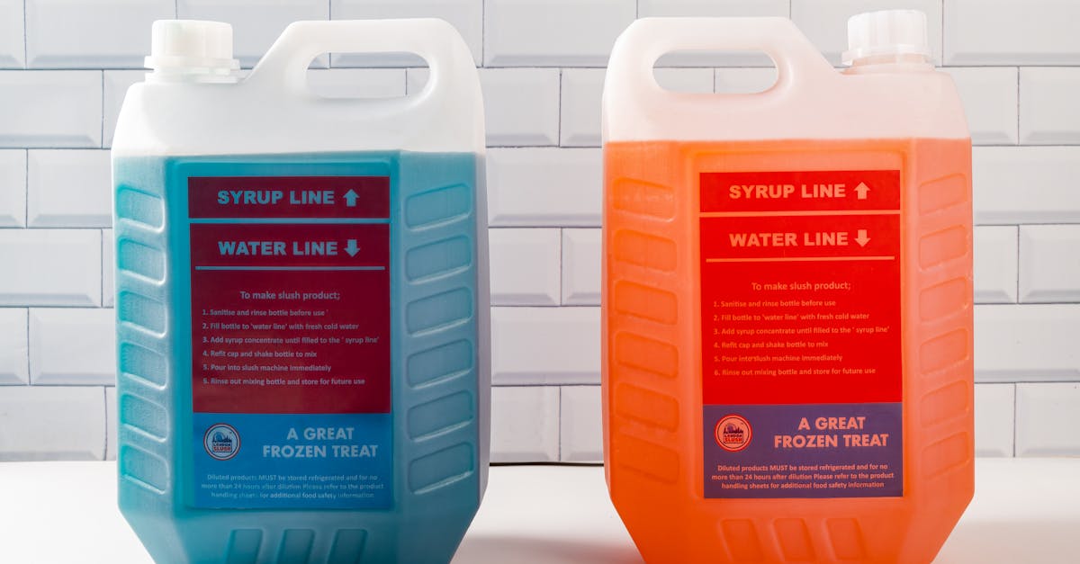 two large plastic containers of blue and orange slush syrup against a white tiled background 1