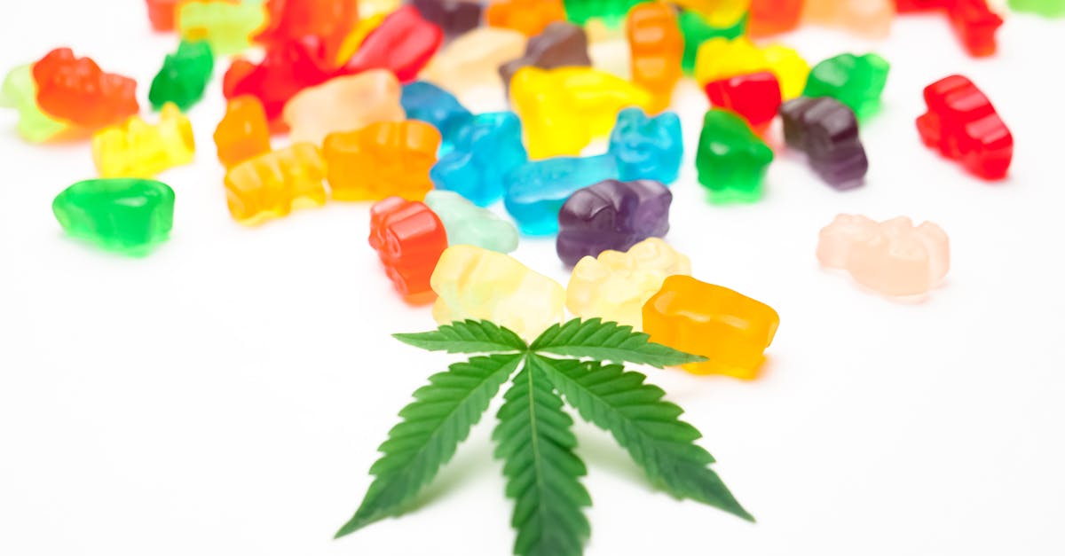vibrant gummy bears scattered alongside a cannabis leaf on a white background